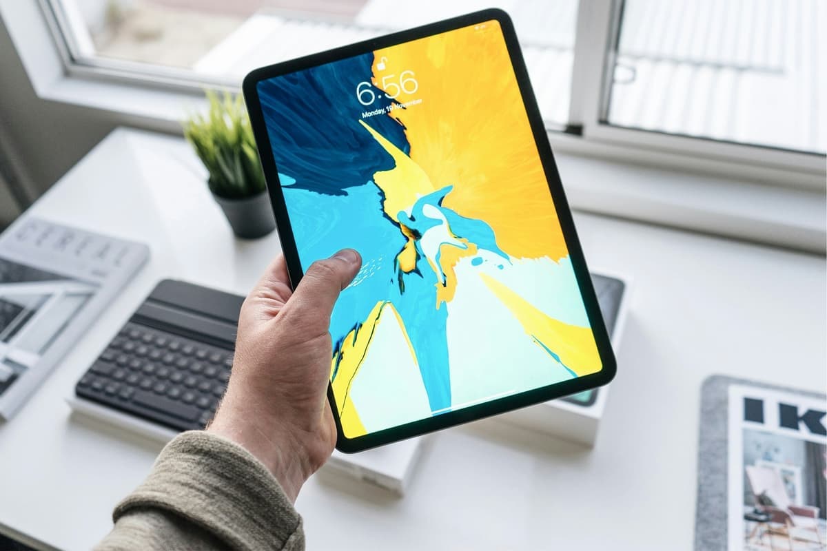 A hand holding an IPad showing its lock screen above a desk with a keyboard